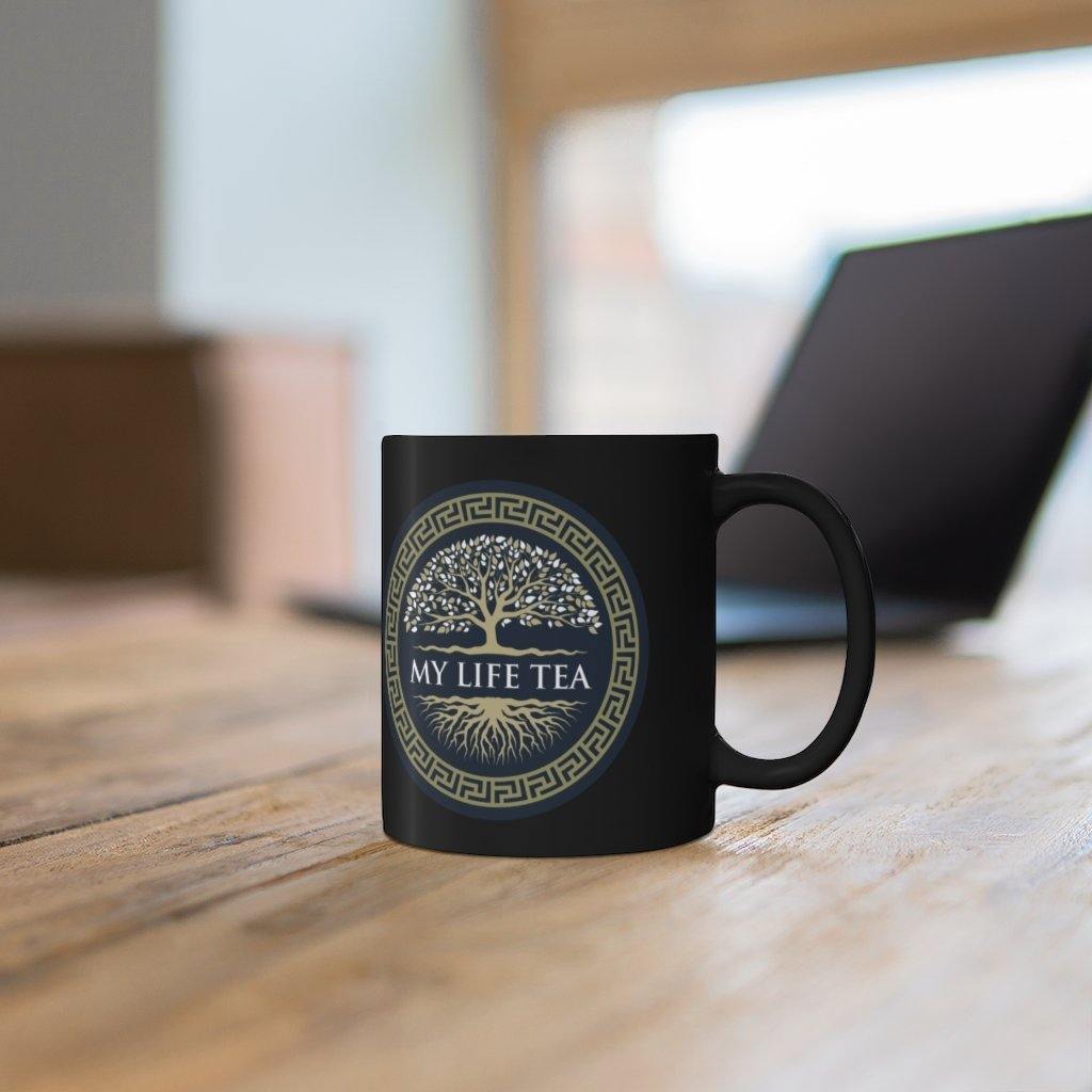 My Life Tea 11oz black mug on a wooden desk beside a laptop